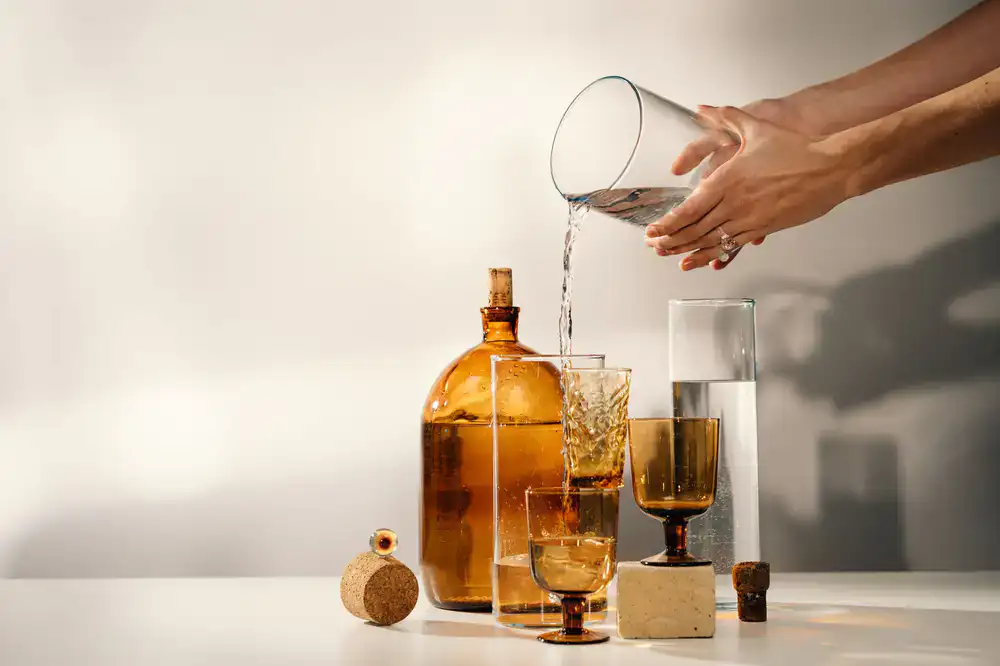 Pouring clear liquid dish soap into a reusable amber glass bottle